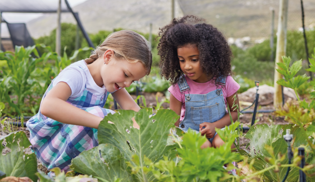 Duas meninas explorando e aprendendo em uma horta orgânica, evidenciando a prática de hábitos saudáveis desde a infância.