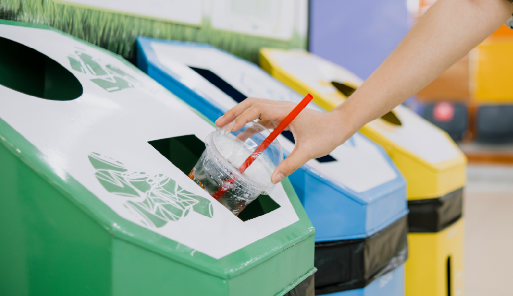 Descarte de copo plástico com canudo em lixeira de reciclagem verde, enfatizando a importância do descarte adequado para reciclabilidade.